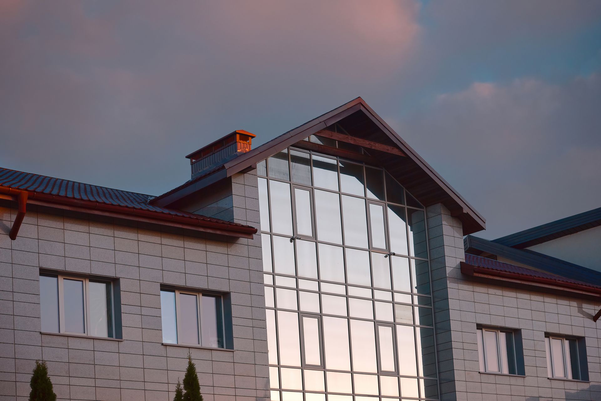 Modern building facade with large glass atrium under a cloudy sunset sky