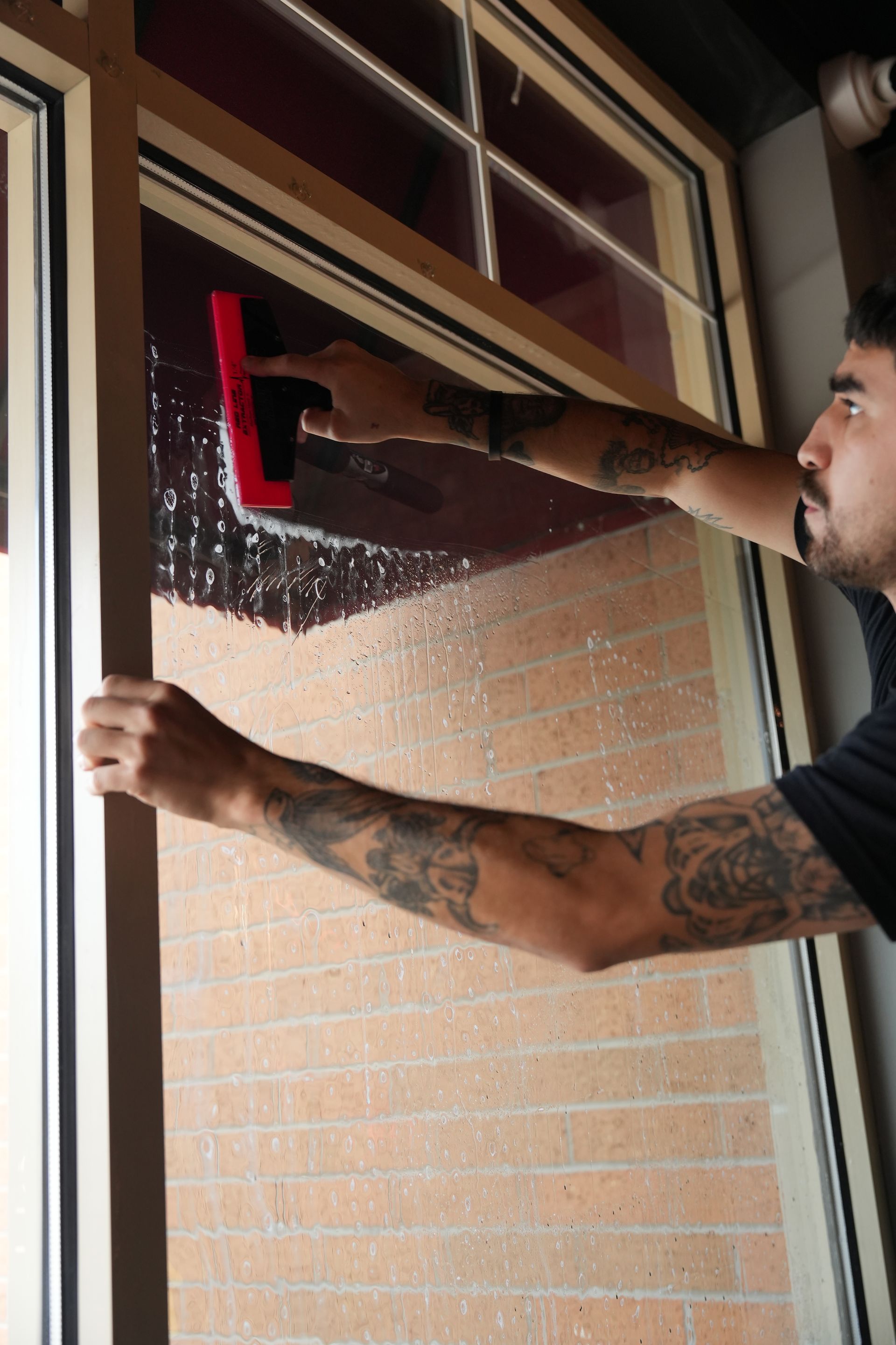Person cleaning a large window with a yellow squeegee, leaving streaks of water behind.