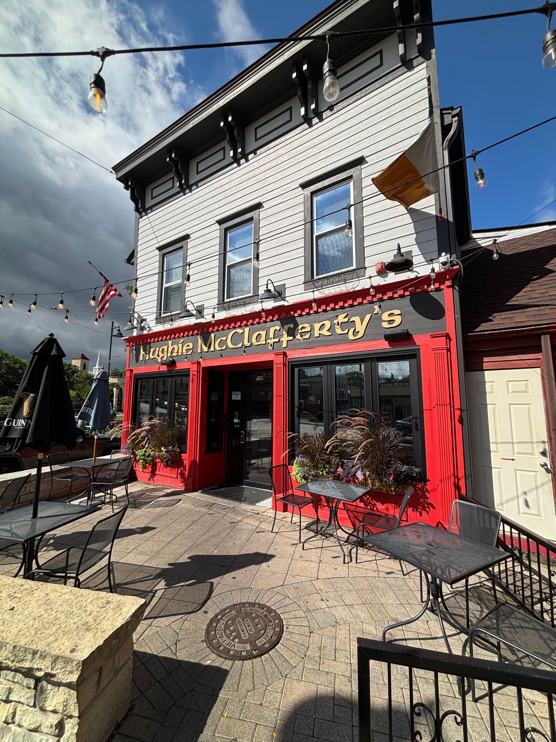 Red storefront bakery/cafe on a sunny street corner with white upper facade and patio seating