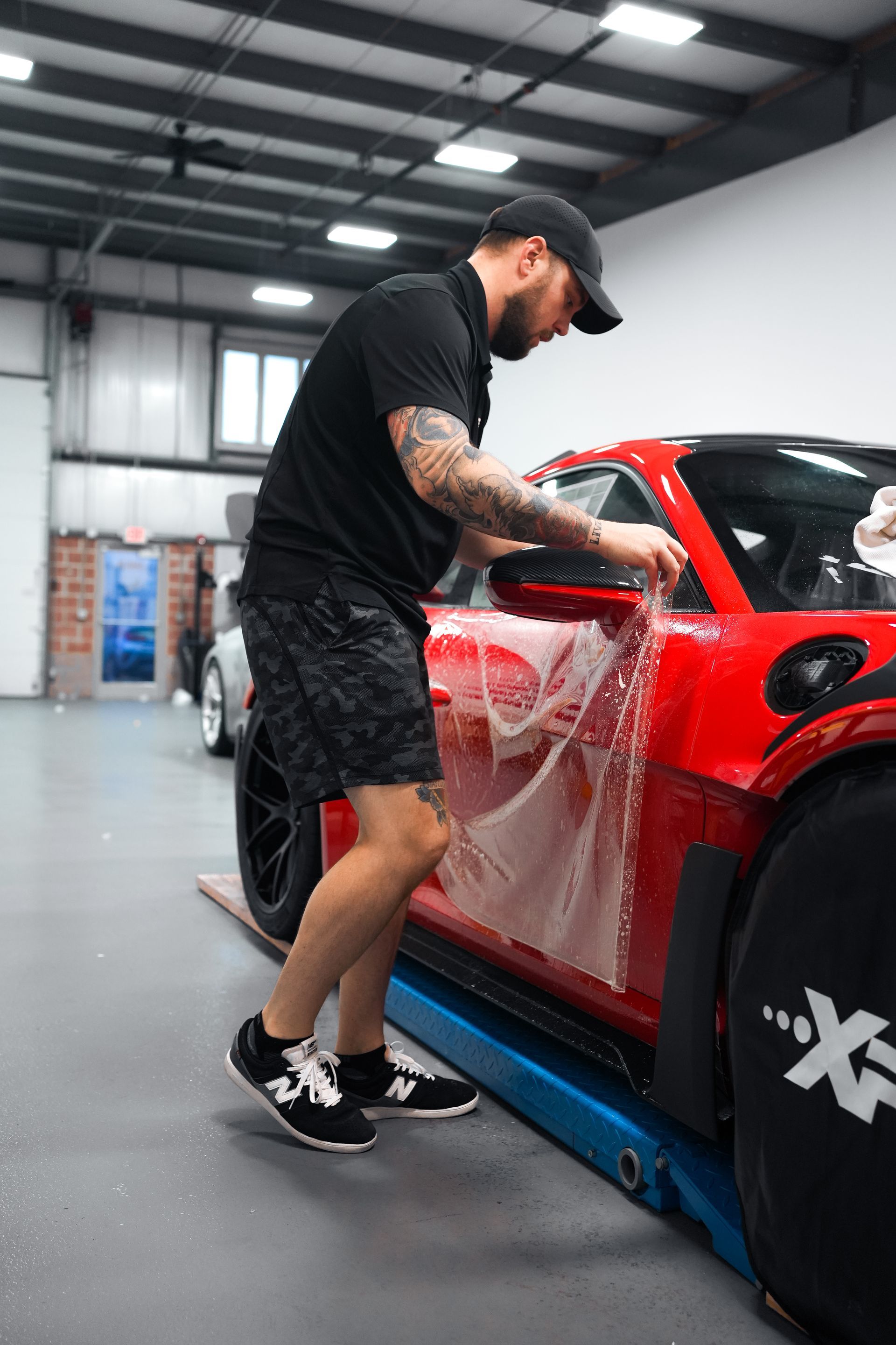 Man wrapping clear protective film on a red sports car in a workshop