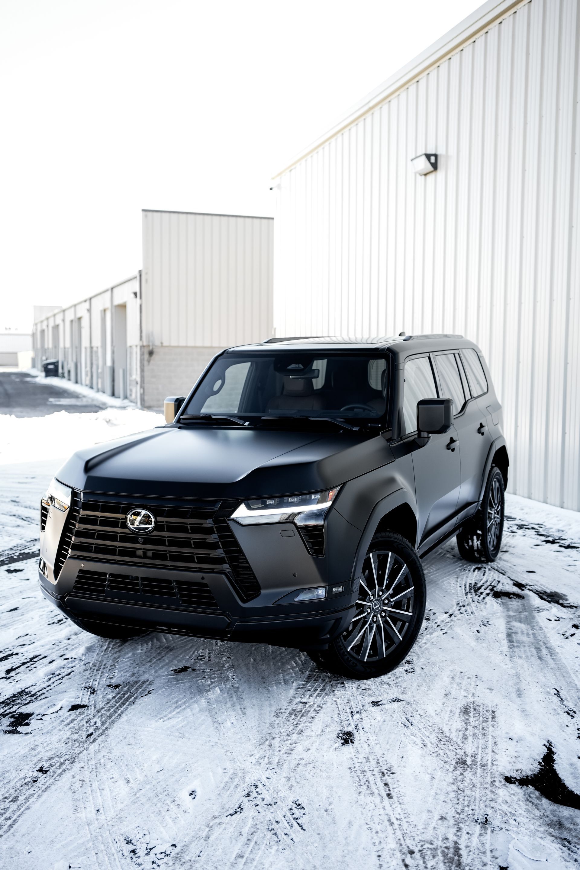 Black SUV parked on a snowy industrial lot beside white warehouse buildings