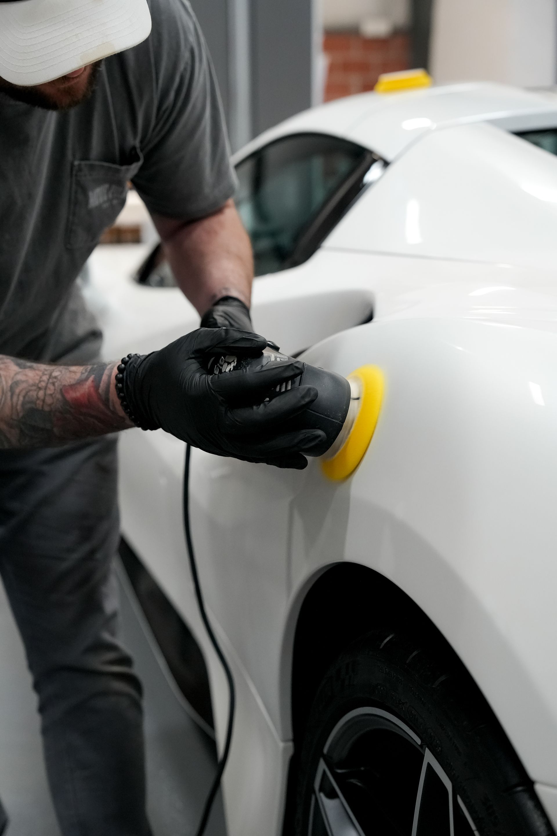 Person polishing a white car with a yellow buffer in a garage