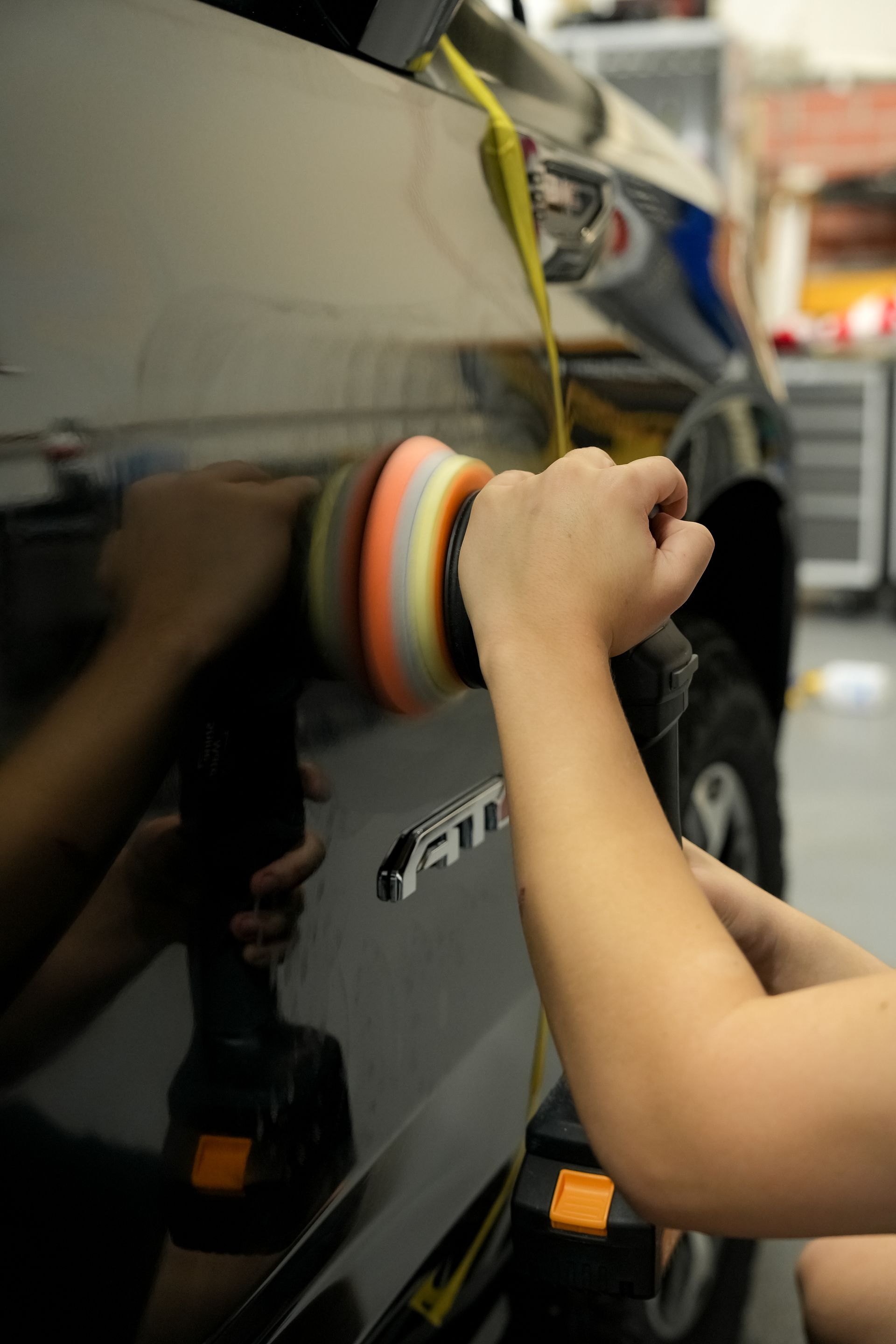 Person polishing a black car with a multicolored buffer in a garage