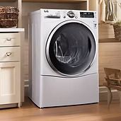 White LG front-load washing machine in a laundry room, next to a cabinet.