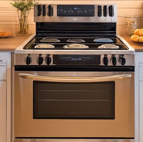 Stainless steel slide-in gas range with five burners, front control knobs, and a digital display in a kitchen setting.
