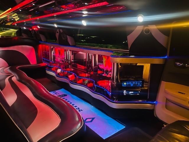Red-lit luxury limousine interior with plush seating, bar area, and neon lighting