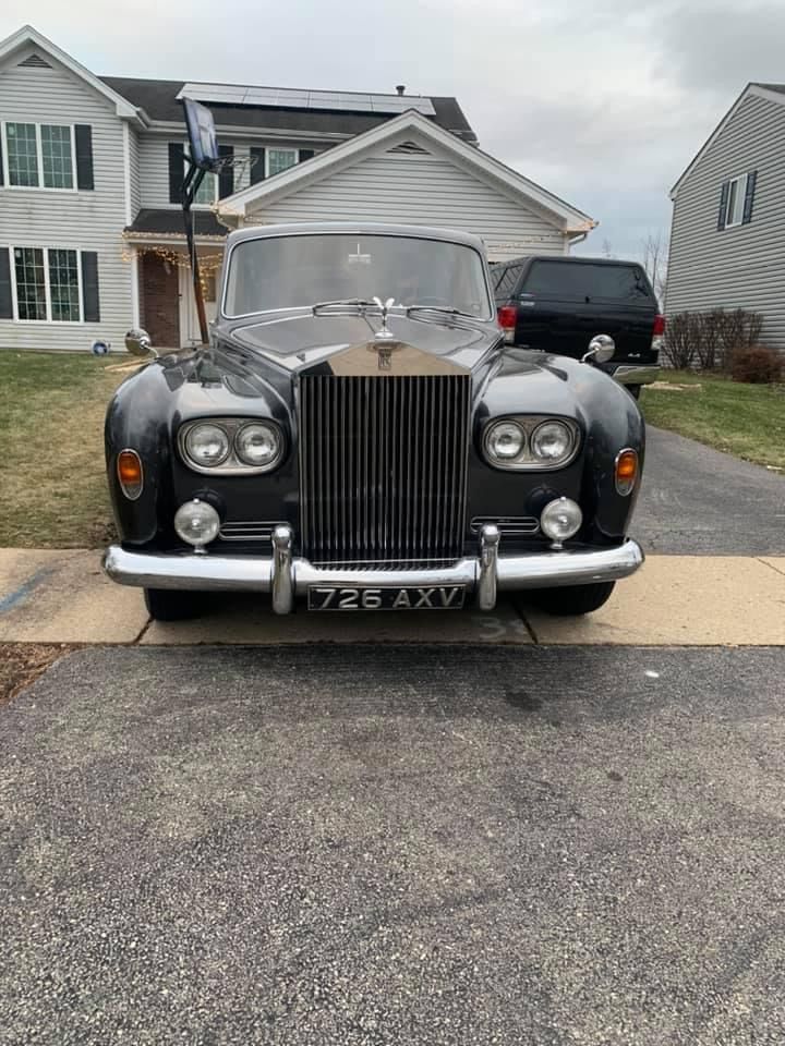 Front view of a black classic Rolls-Royce parked in a suburban driveway, with the hood open.