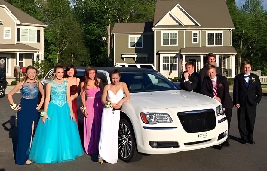 Group dressed for prom posing beside a white limousine in a suburban driveway
