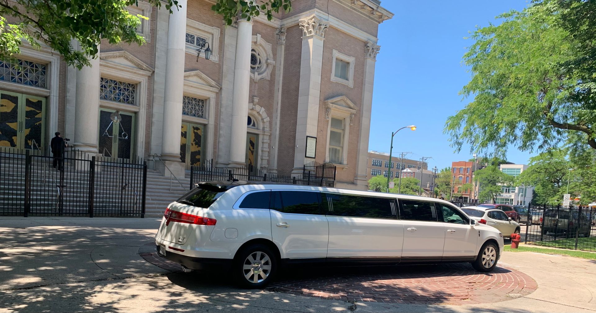 White stretch limousine parked beside a historic building on a sunny street