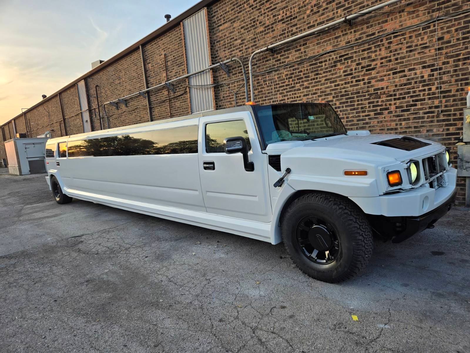 White stretched Hummer limousine parked beside a brick building at dusk