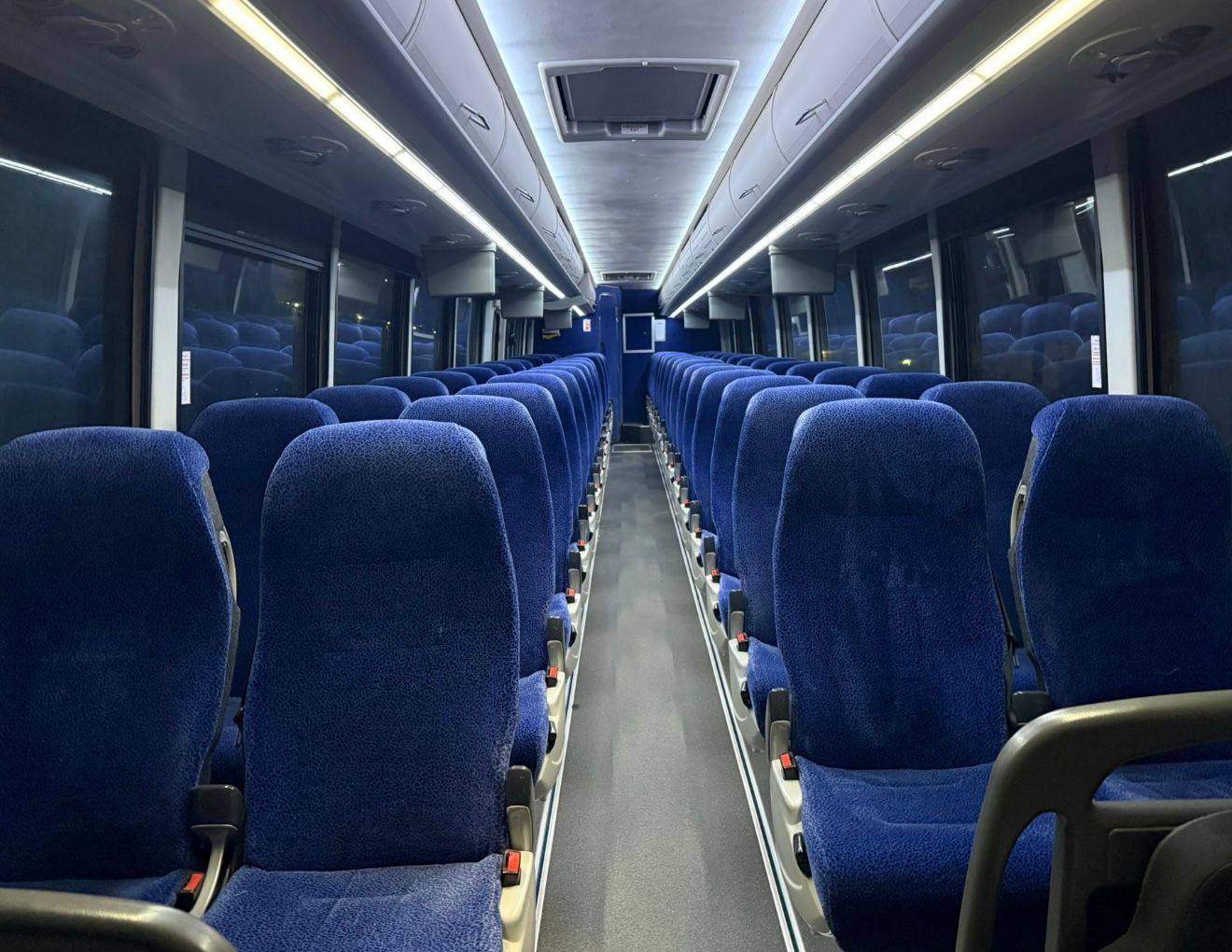 Empty train carriage with rows of blue seats and overhead lights
