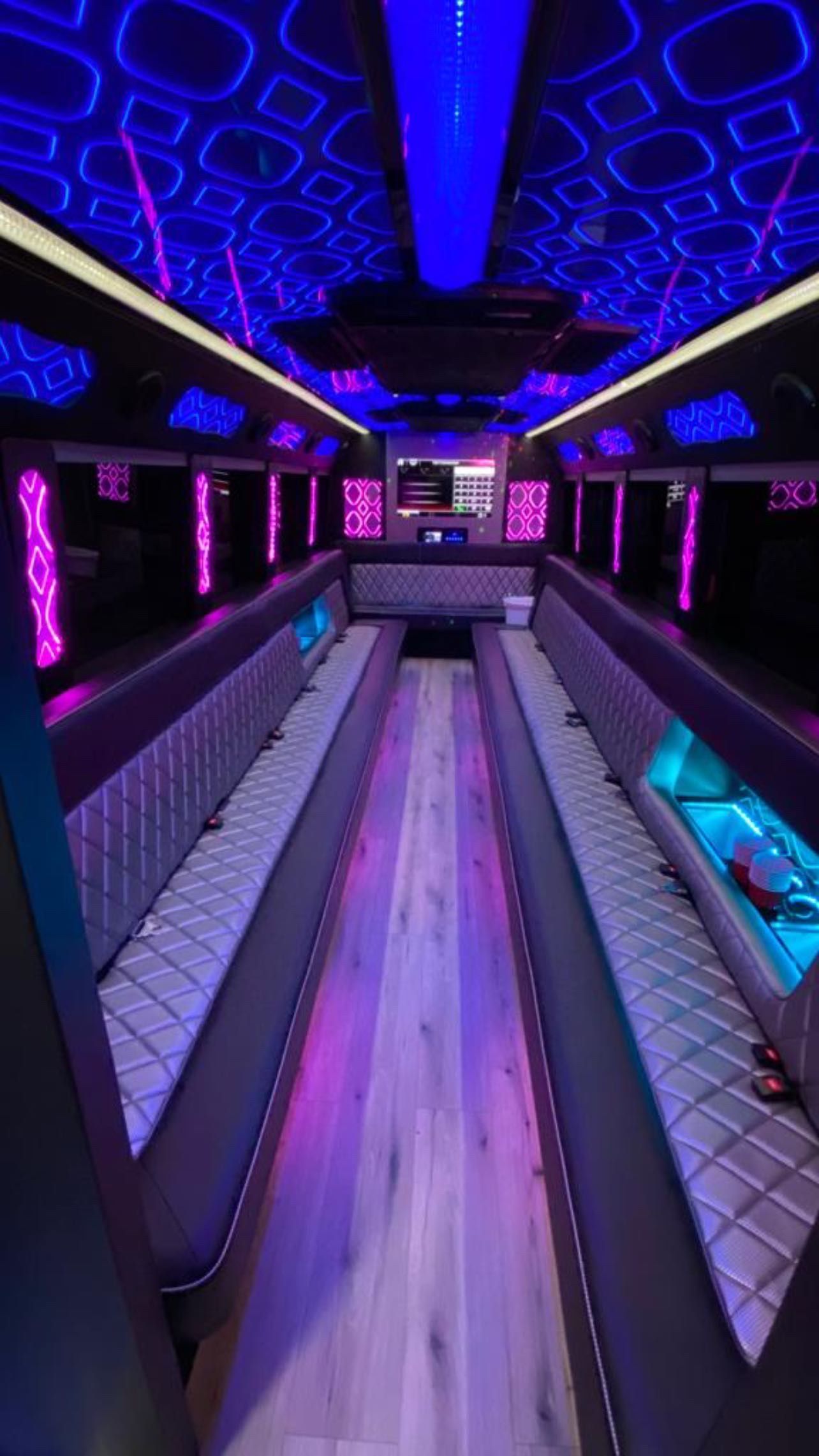 Neon-lit party bus interior with purple ceiling lights, bench seating, and a central aisle