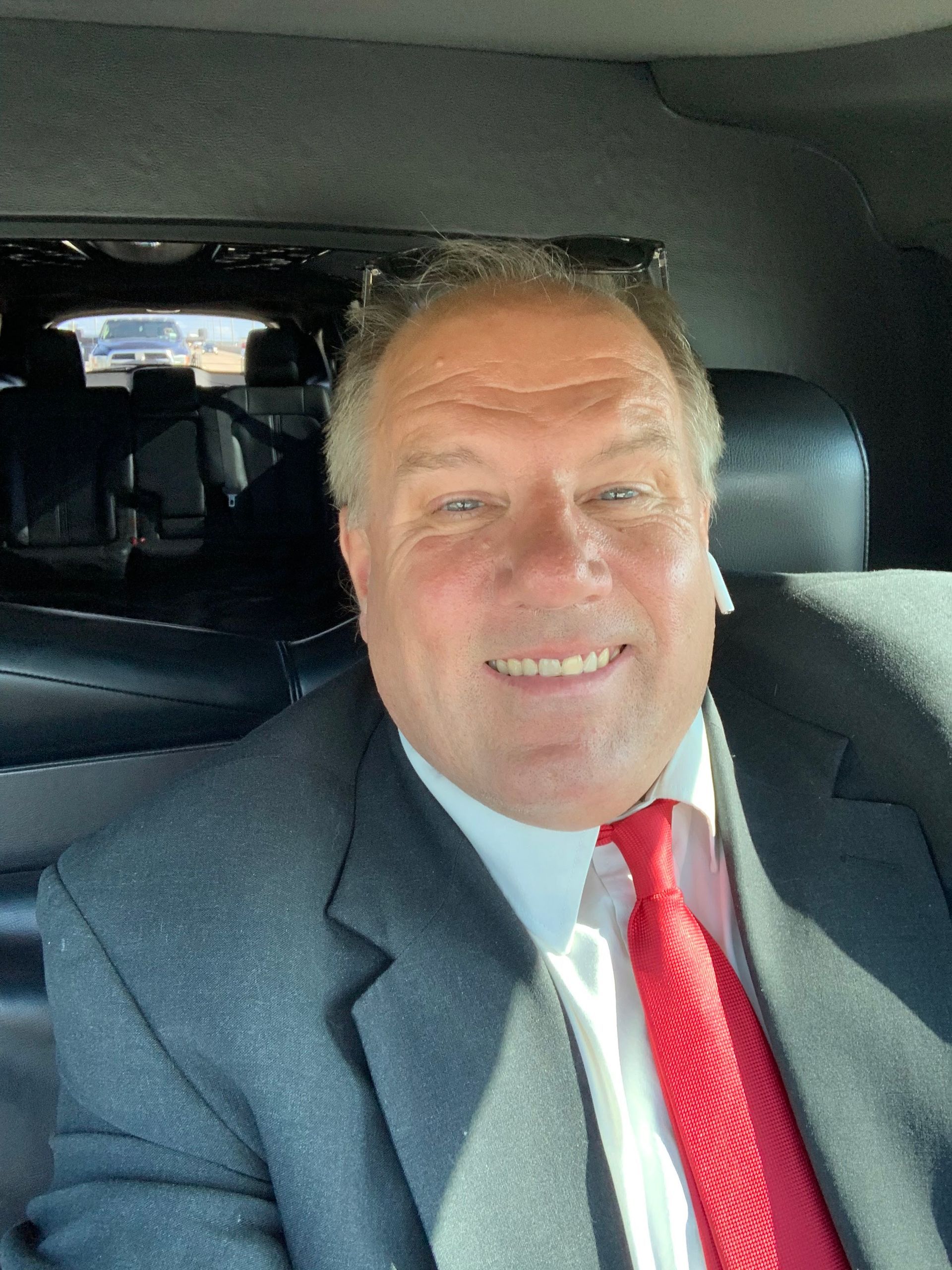 Smiling man in a gray suit and red tie seated in a car