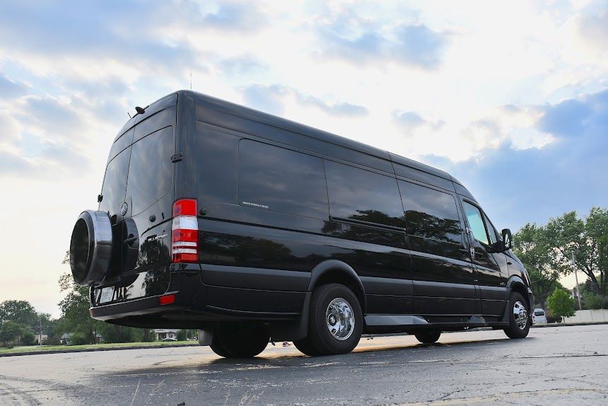 Black extended van parked on pavement under a cloudy sky, rear and side view