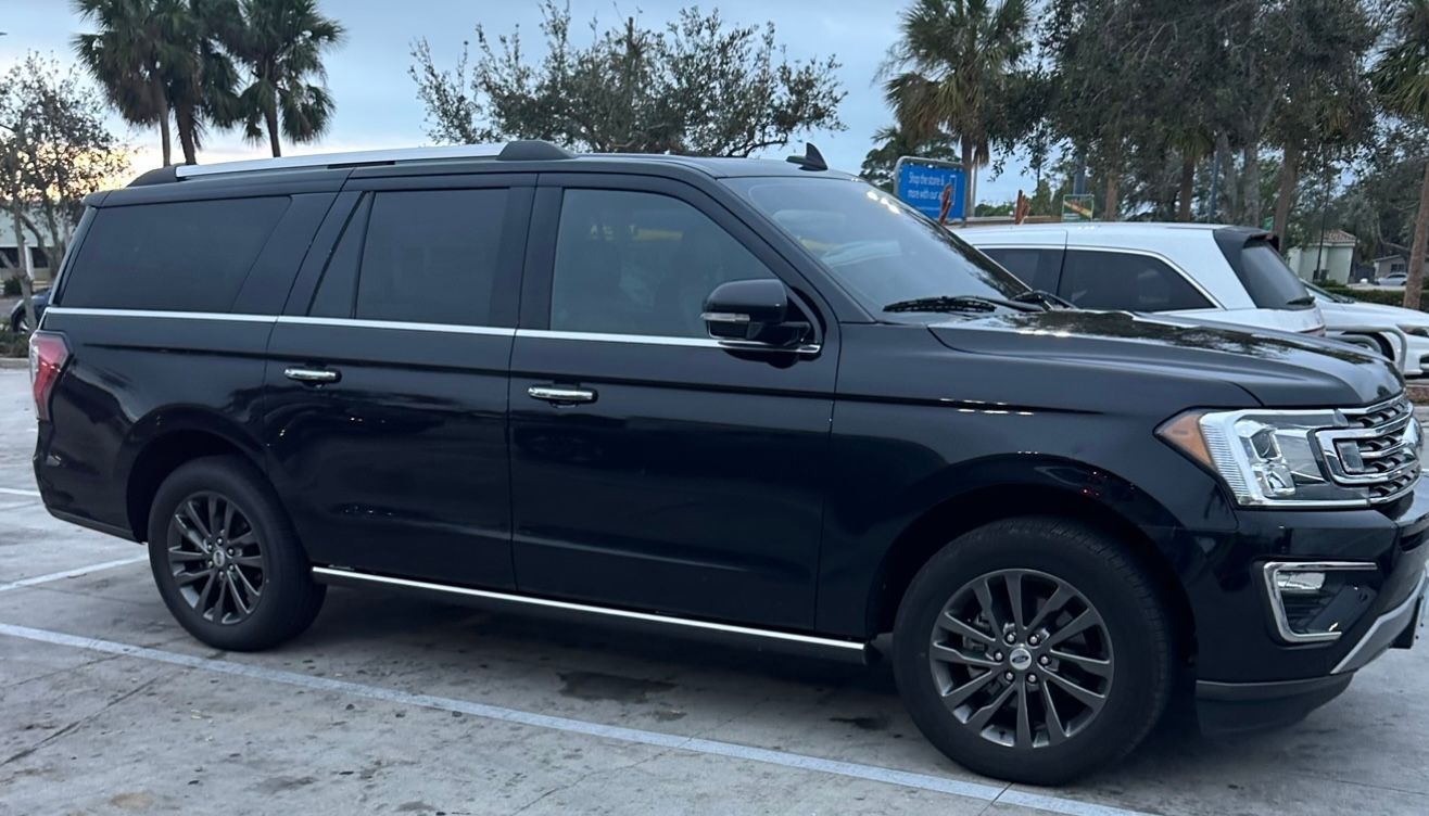 Black SUV parked in a lot, side view, with palm trees and other cars in the background