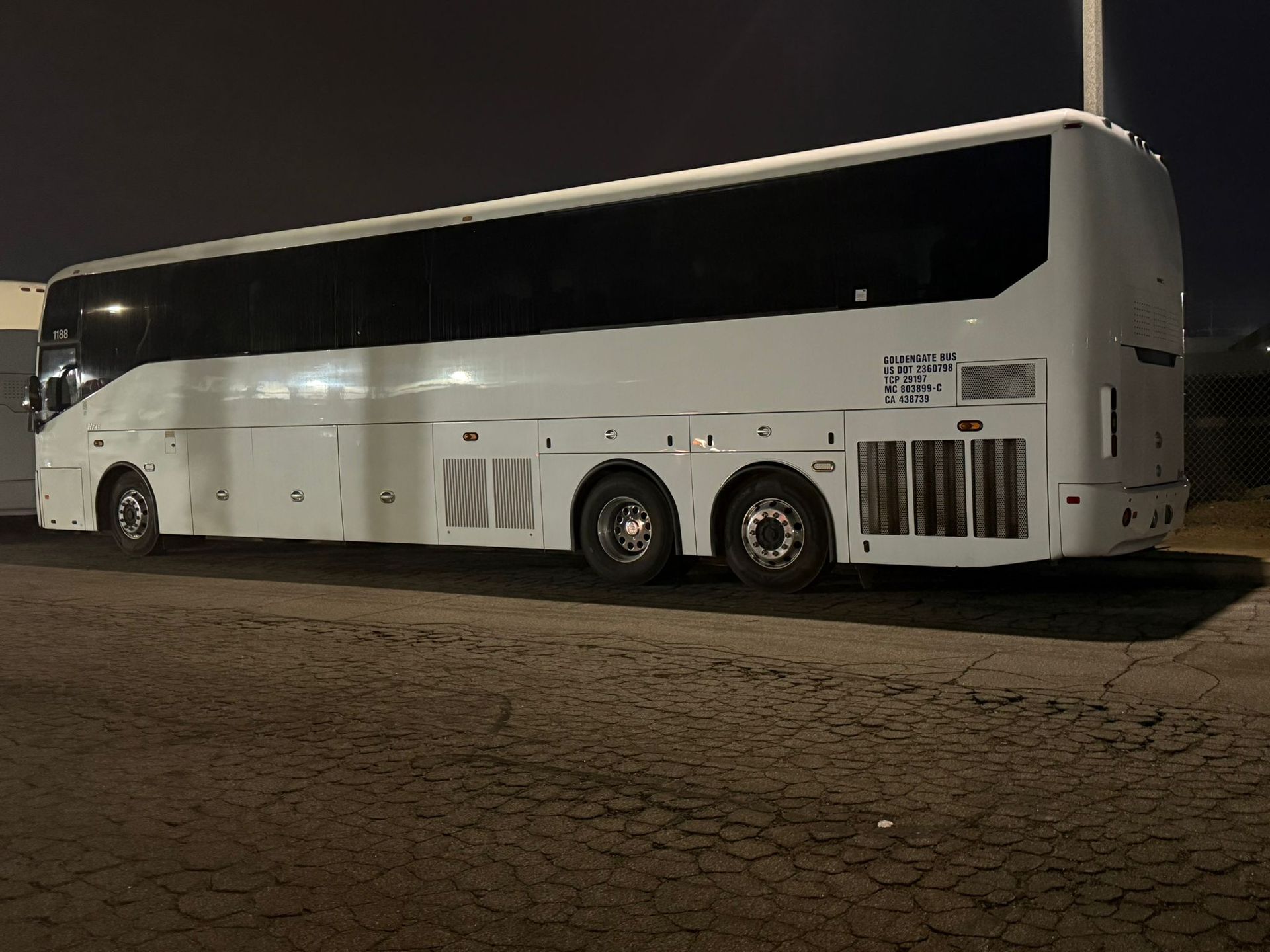 White double-decker coach bus parked at night on a cracked road, side view.