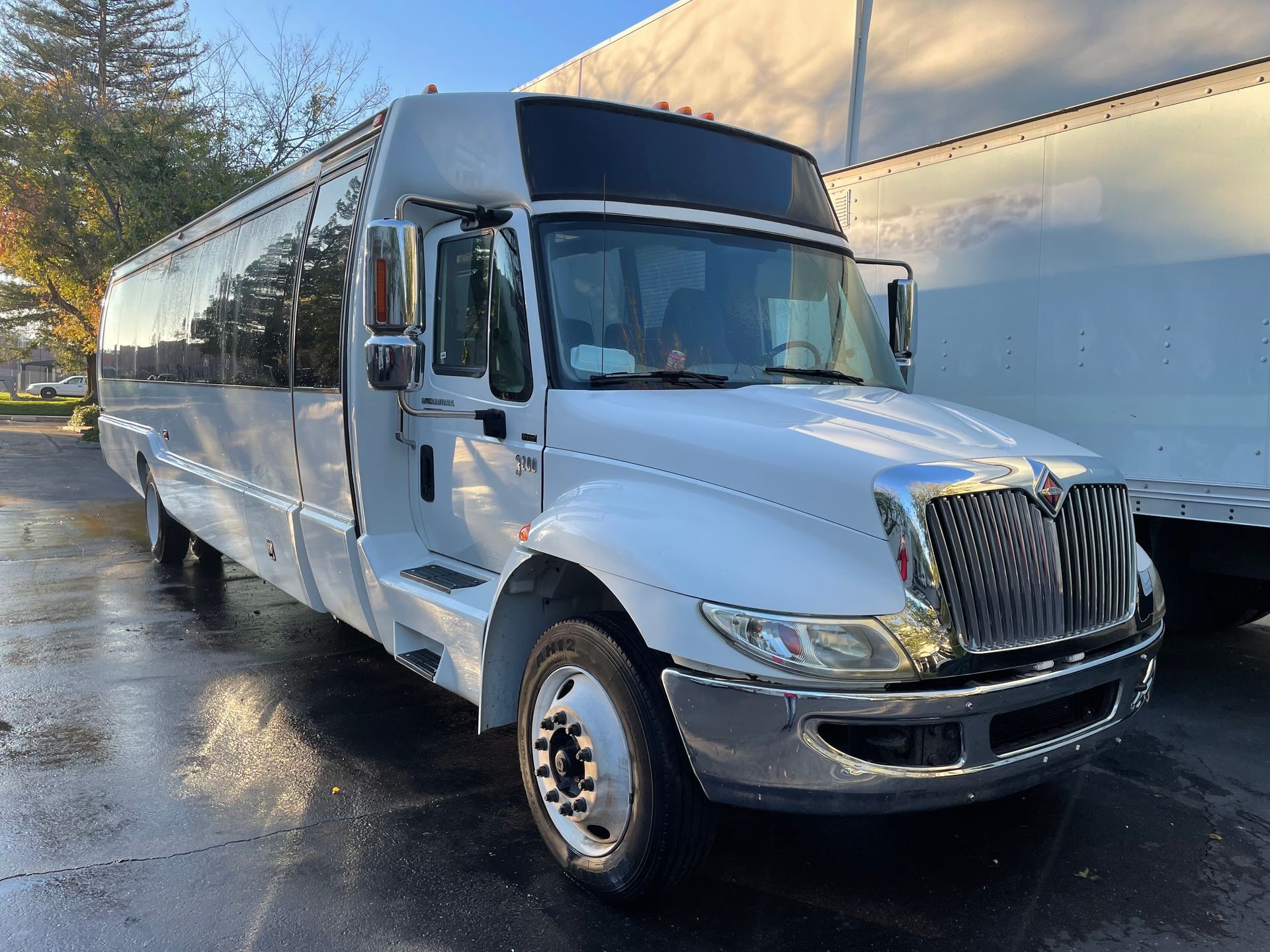 White coach bus parked on a wet street beside a building in daylight