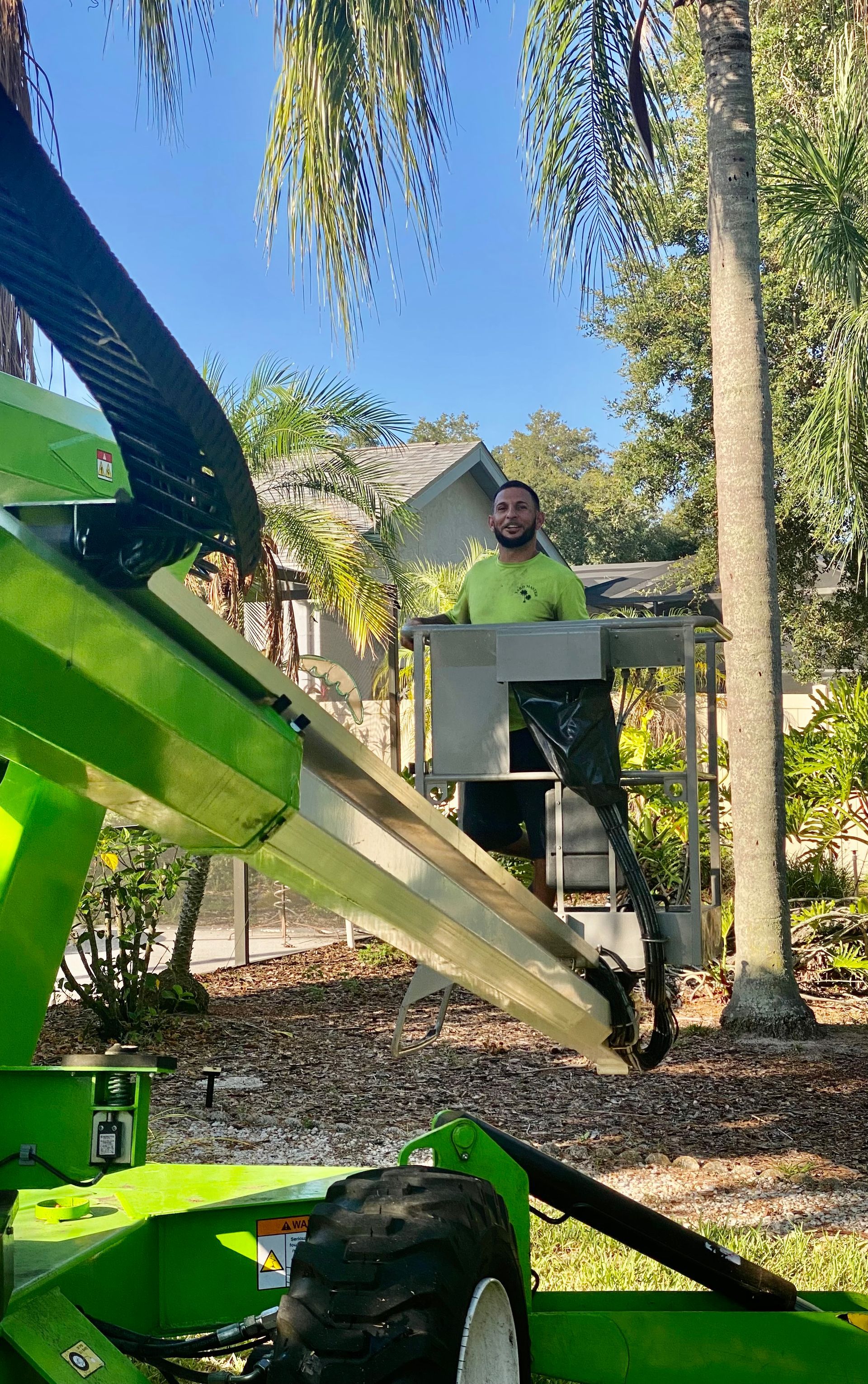A man is standing on top of a green machine cutting a tree.