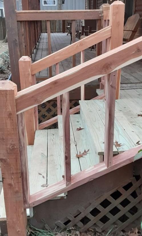 Wooden deck with steps, handrails, and balusters. New light wood decking contrasts with the reddish-brown cedar rails.