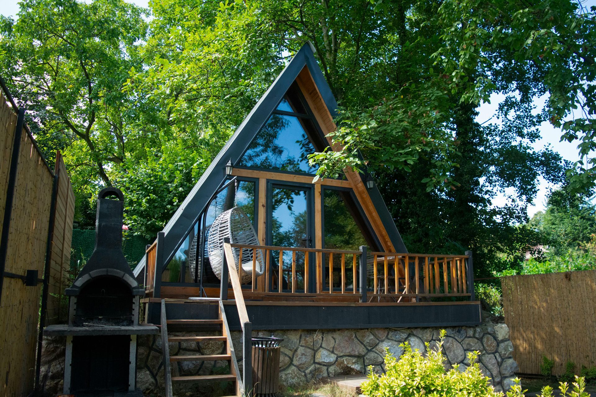 A small triangle shaped house with a balcony and stairs leading up to it surrounded by trees.