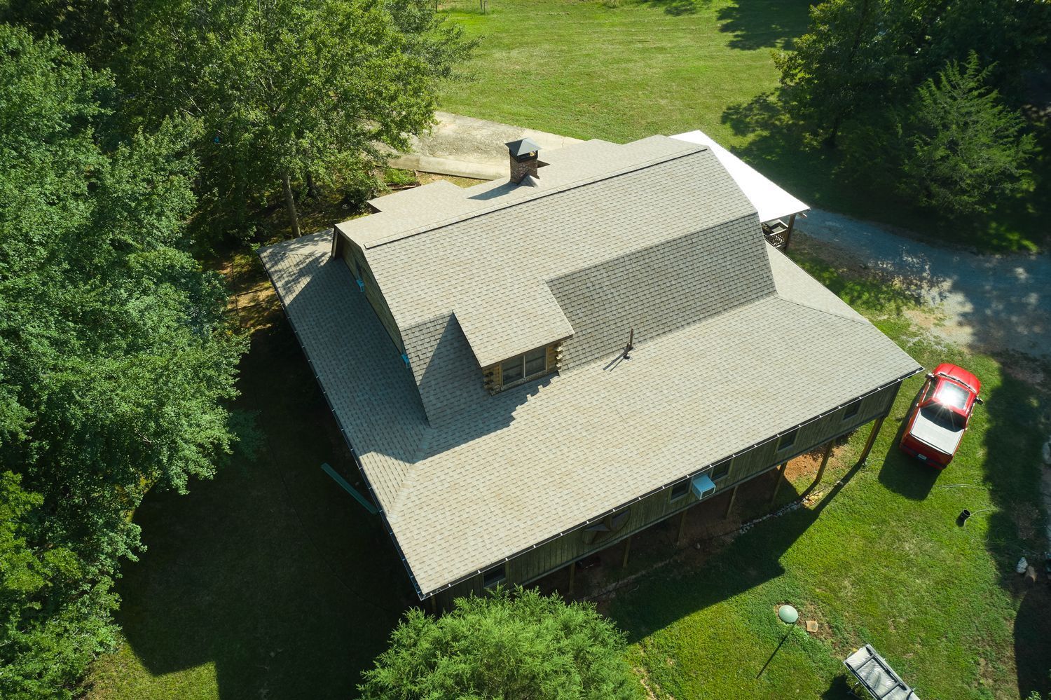 Overhead view of a house with a gray roof, surrounded by trees and a parked red car.