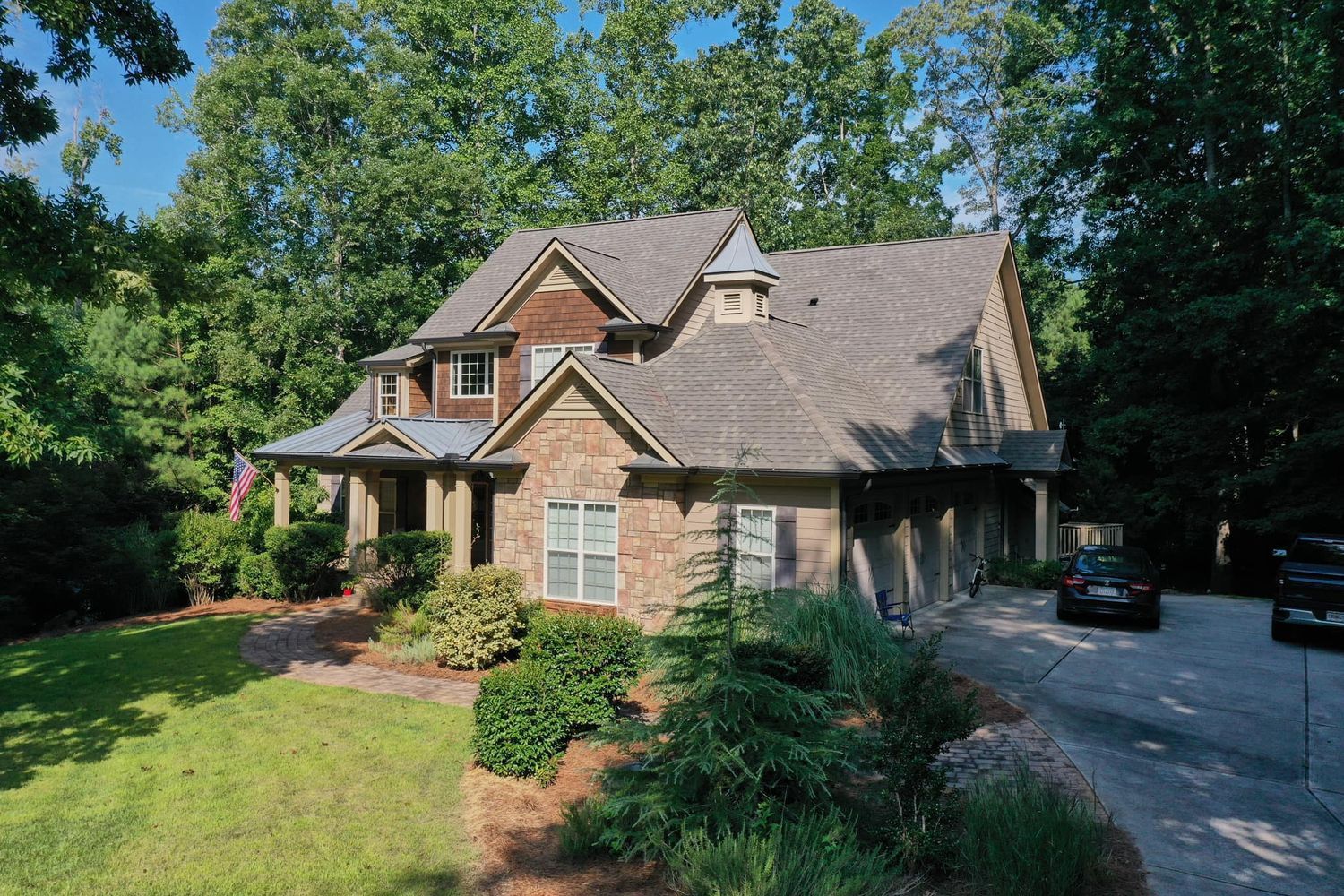 House with brown and tan exterior, surrounded by trees and a driveway.