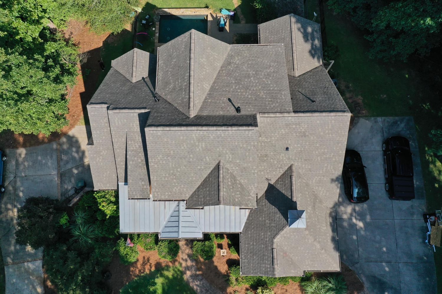 Overhead view of a house with a complex, multi-level gray roof. Two cars parked on the driveway.