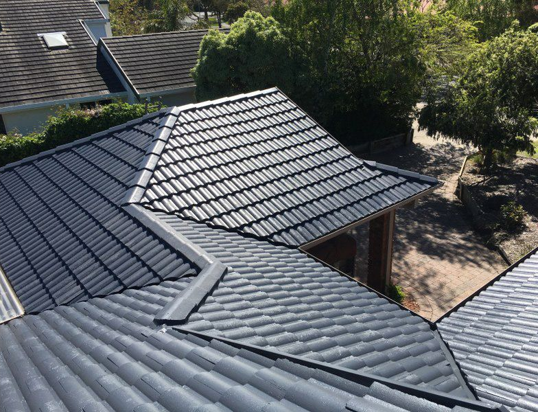 Gray tiled roof with a ridge, a gutter, and a tree in the background.