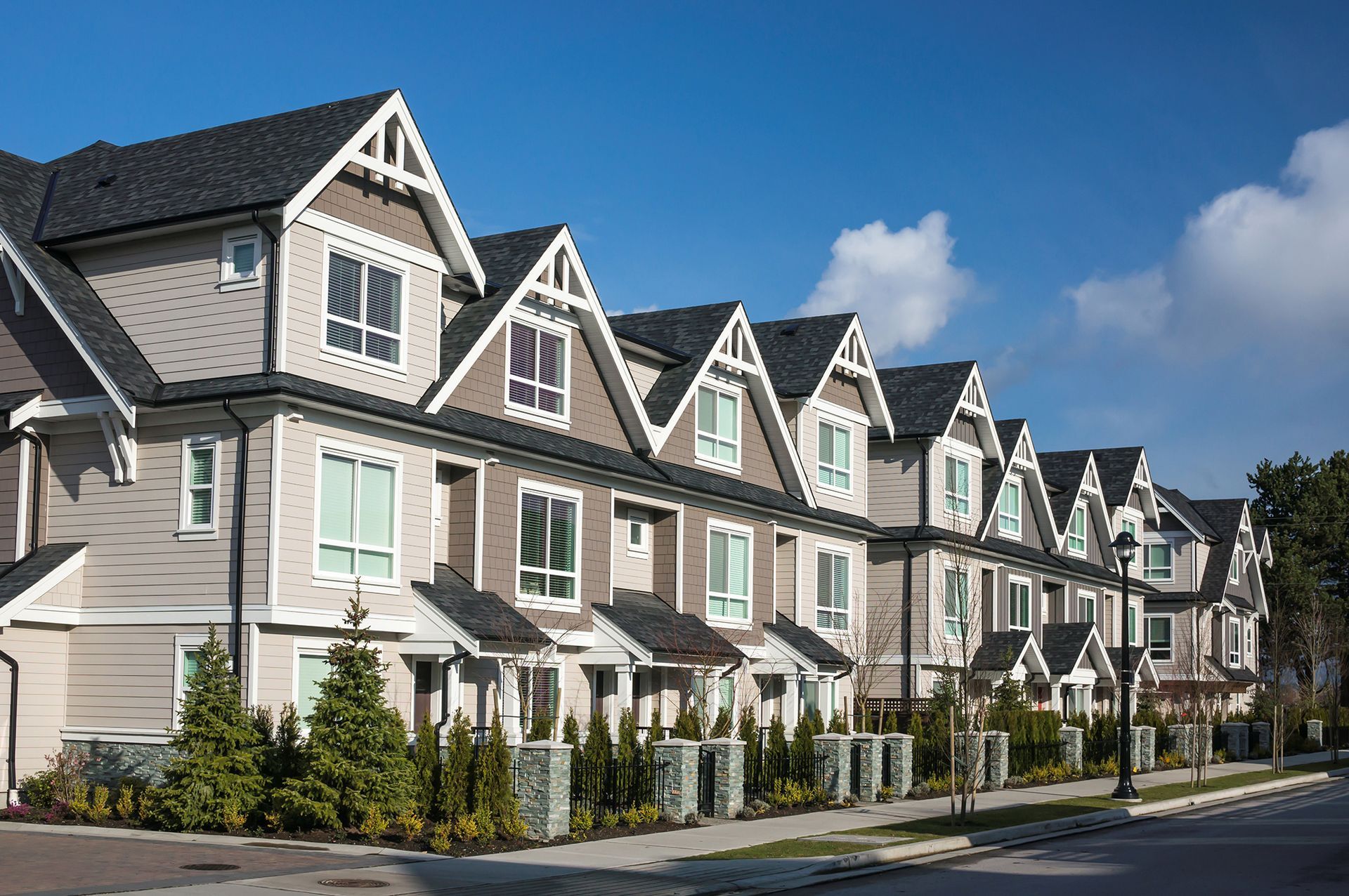 Row of multi-story townhouses with gray siding, black roofs, and white trim against a blue sky.