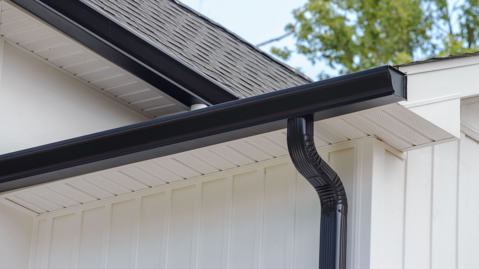 Black rain gutter and downspout on a white house exterior with a gray roof.