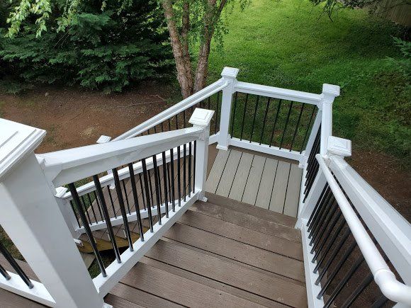 Wooden outdoor staircase with white railings, black balusters, and a green backdrop.