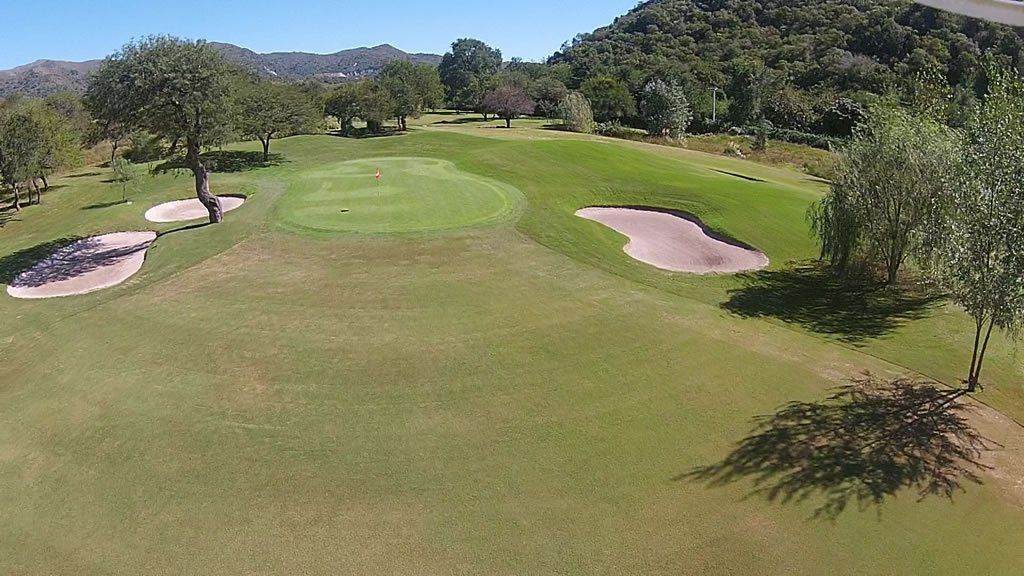 Una vista aérea de un campo de golf con árboles y bunkers.