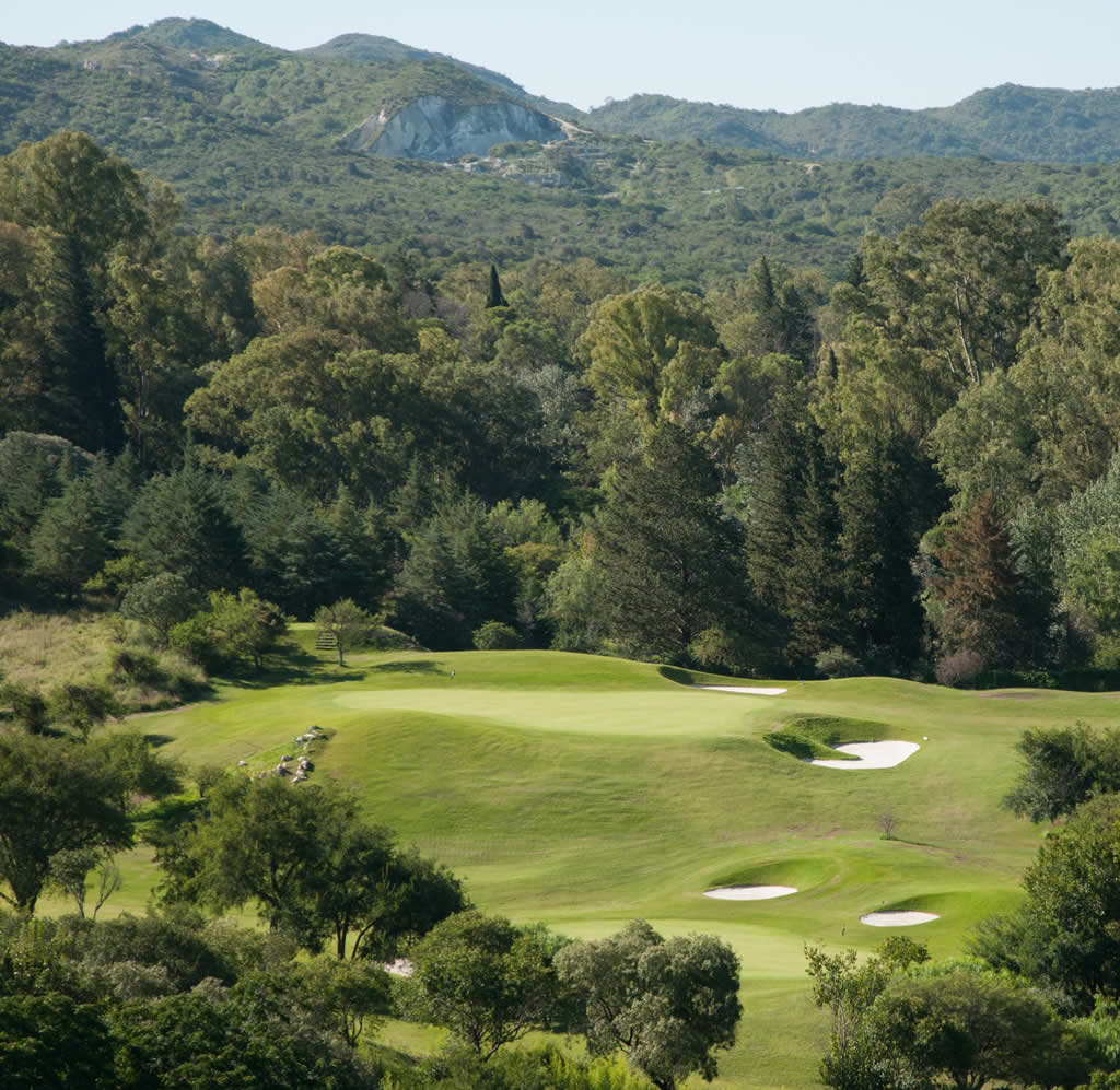 Un campo de golf con árboles y montañas al fondo.