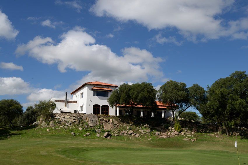 Una gran casa blanca se encuentra en la cima de una colina junto a un campo de golf.