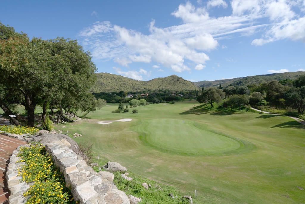 Un campo de golf con árboles y montañas al fondo.