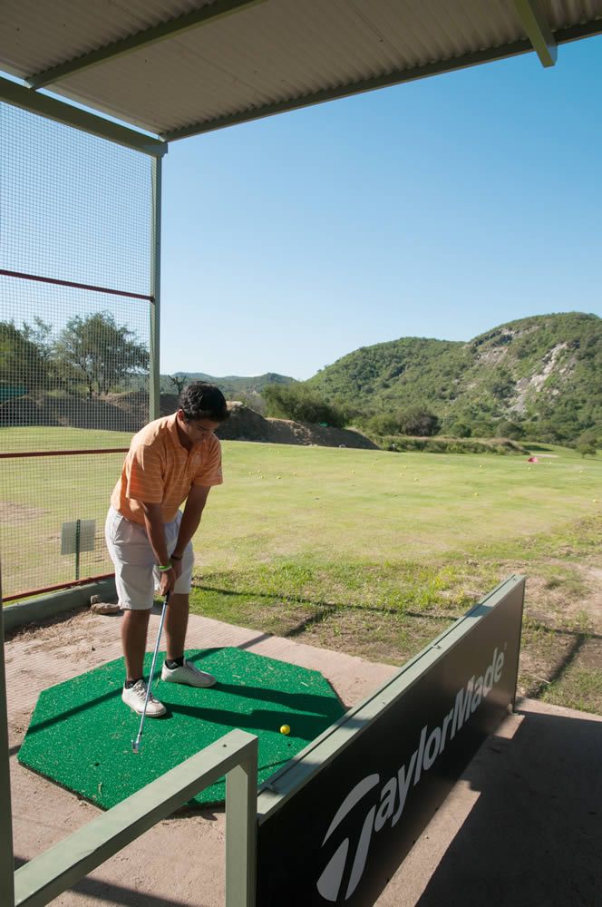 Un hombre está haciendo pivotar un palo de golf sobre una alfombra verde en un campo de golf.