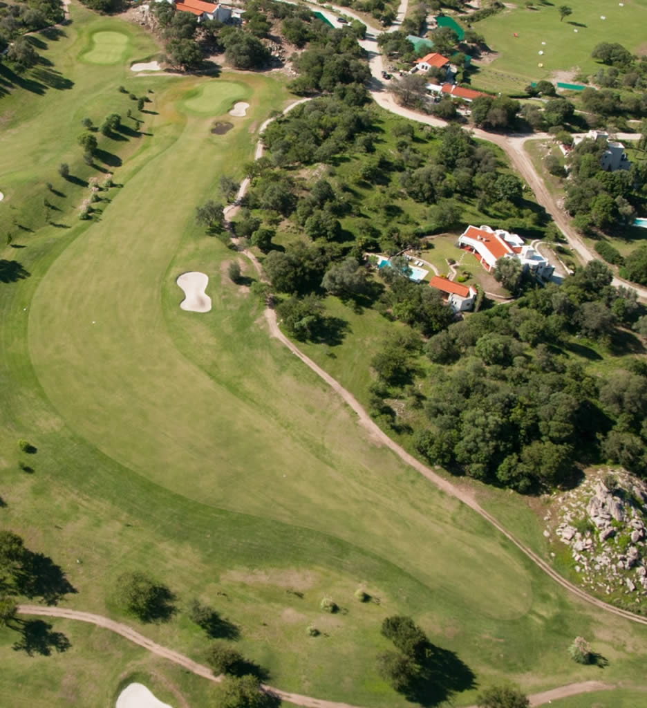 Una vista aérea de un campo de golf con árboles y casas al fondo.
