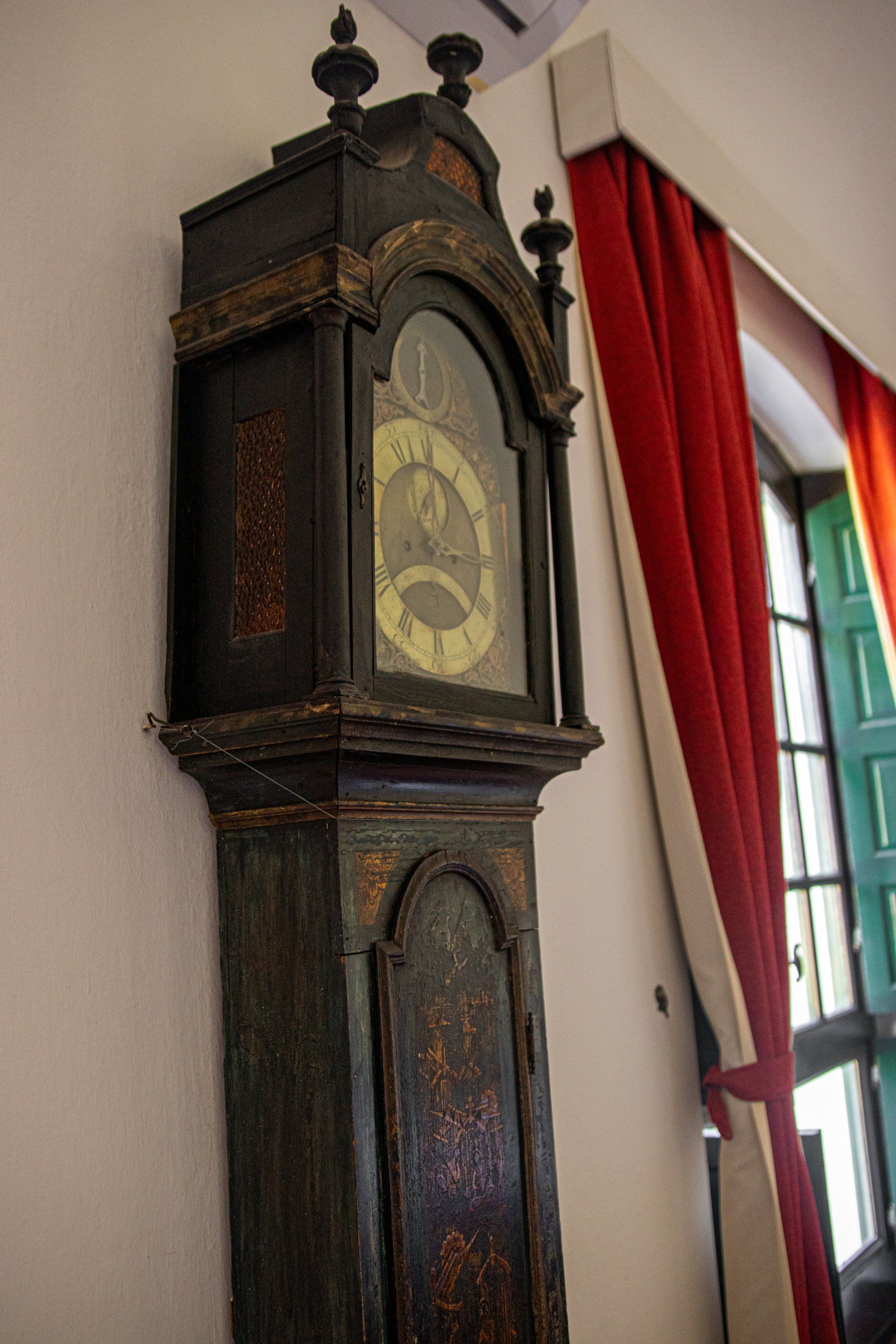 Un reloj de pie está colgado en una pared junto a una ventana.