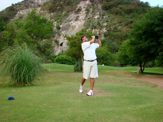 Un hombre está haciendo swing con un palo de golf en un campo de golf.
