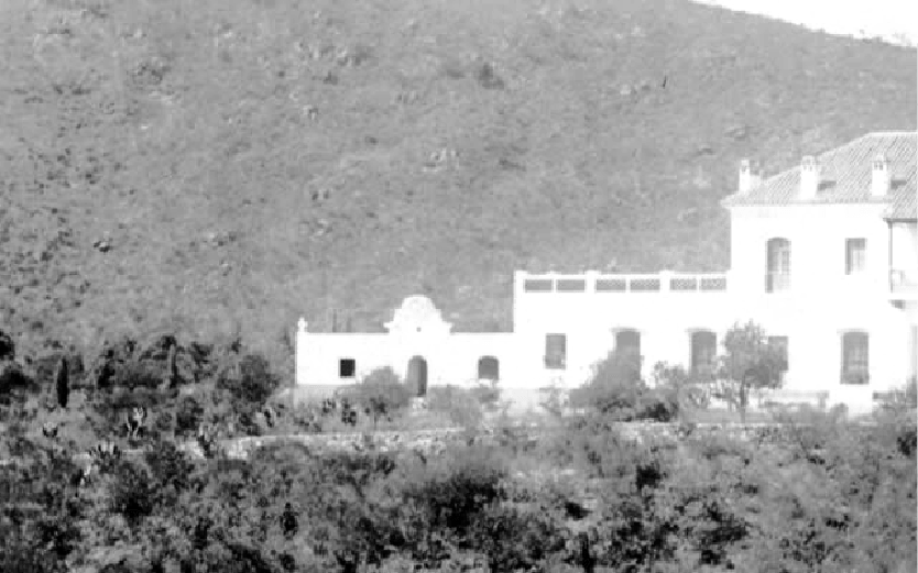 Una fotografía en blanco y negro de un gran edificio blanco en la cima de una colina rodeada de árboles.