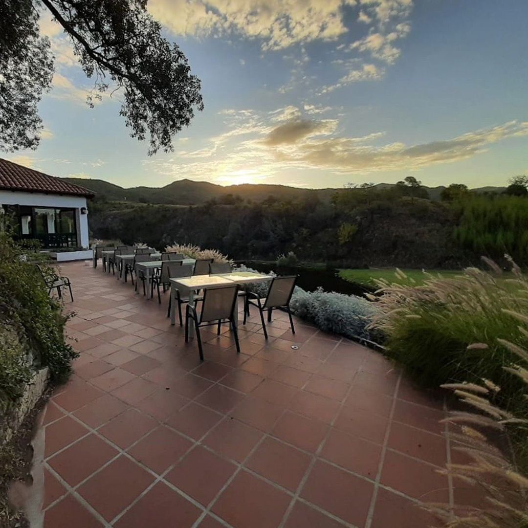 Un patio con mesas y sillas y un atardecer de fondo.