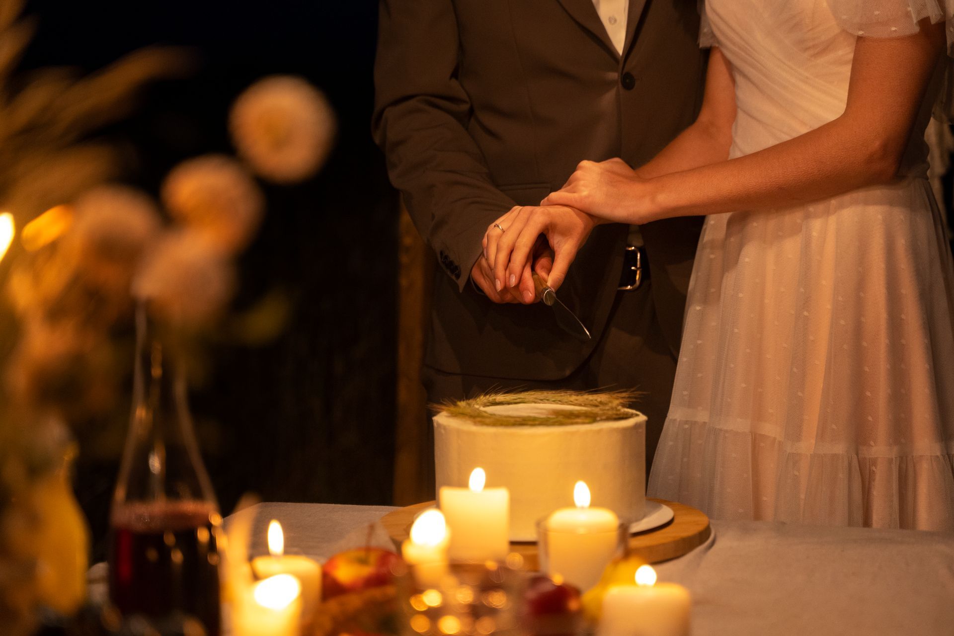 Una novia y un novio están cortando su pastel de bodas con velas al fondo.