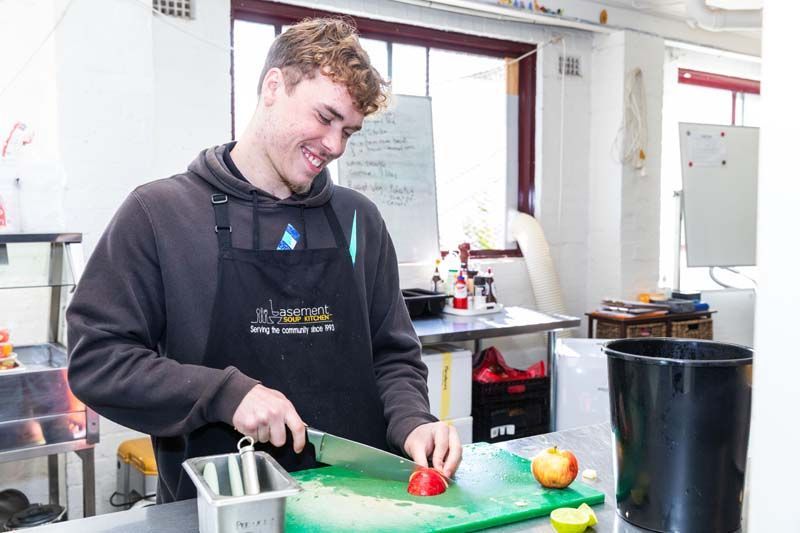 Person chopping a red pepper on a green cutting board in a kitchen classroom