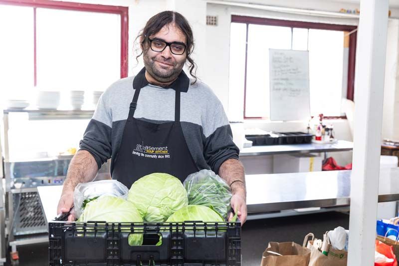 Man in apron standing behind crates of green cabbages in a kitchen or market prep area