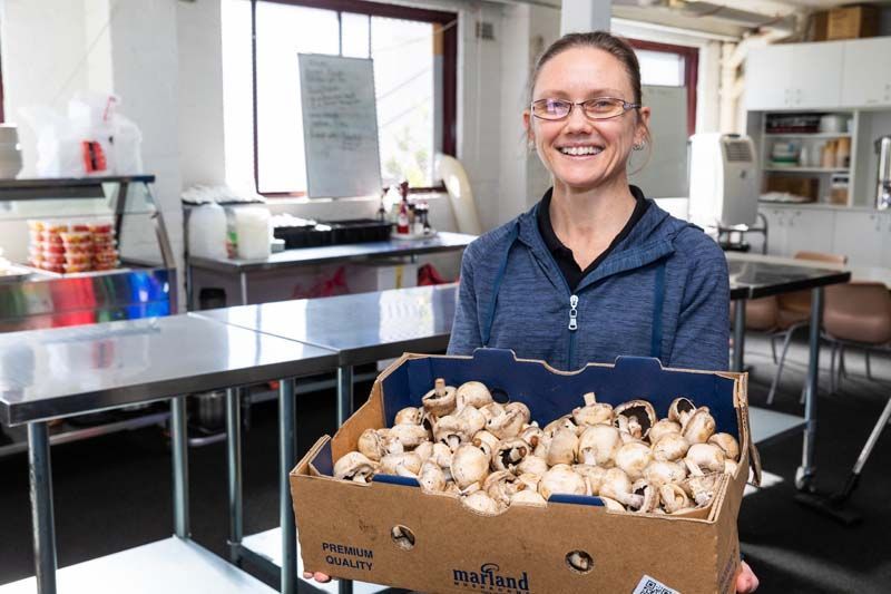 Person smiling and holding a box of mushrooms in a kitchen workspace