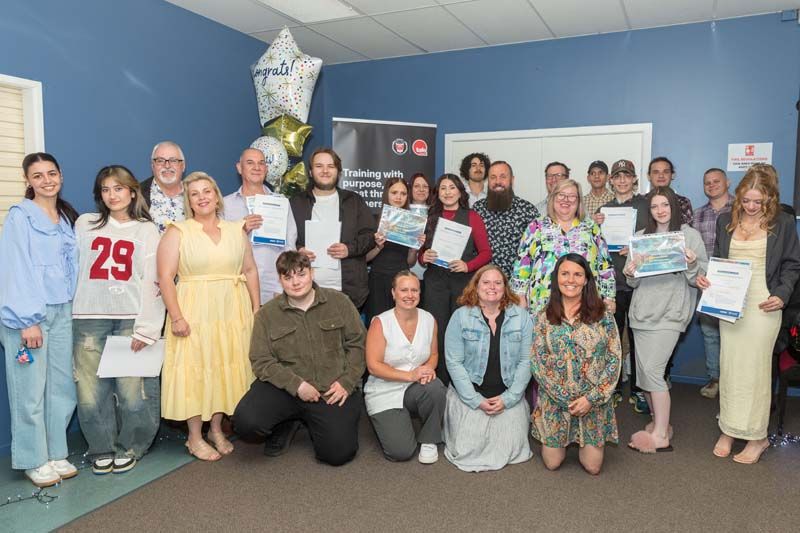 Group of people posing indoors with certificates, smiling in a blue-walled room.