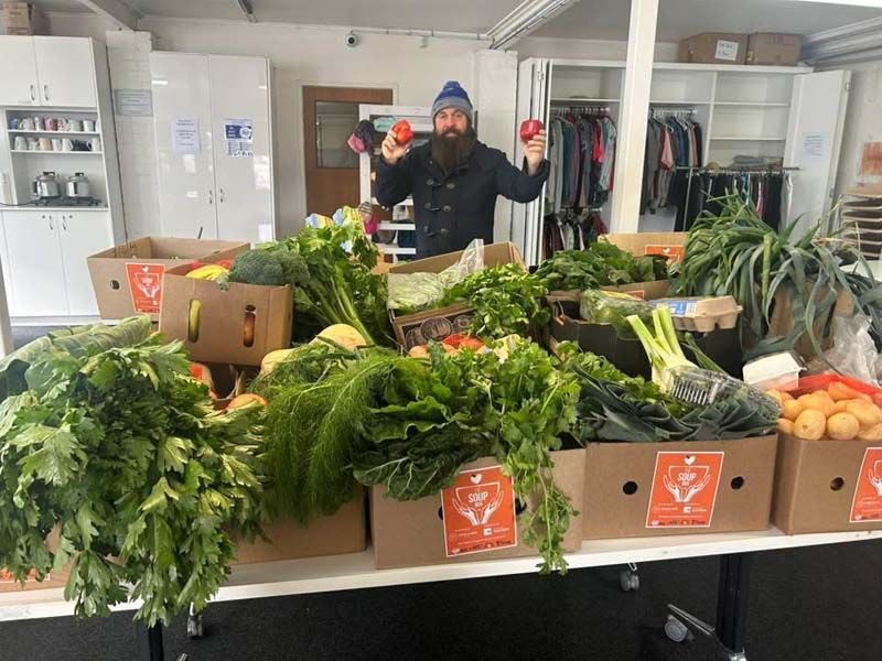 Person behind market produce display with leafy greens and vegetables in a room.