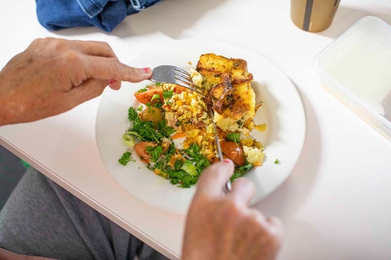 Hands eating a plated meal with herbs and potatoes at a table