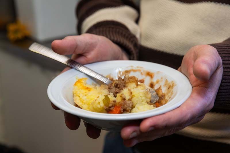 Hands holding a bowl of mashed potatoes with gravy and a spoon