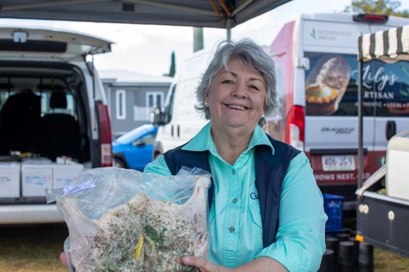 Smiling vendor holding a bag of produce at an outdoor market stall under a canopy